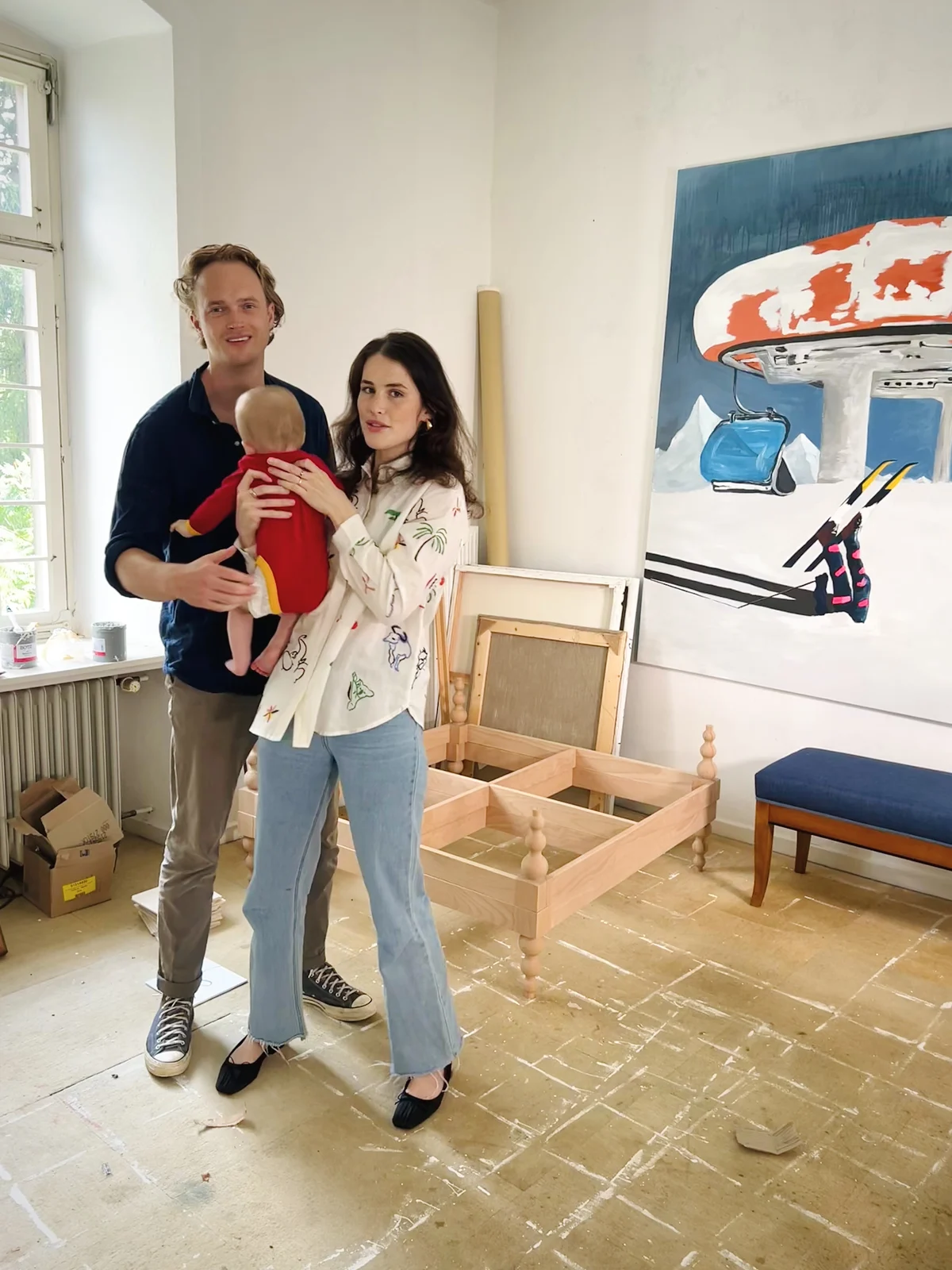 Josephina und Robin Saurma mit ihrem Baby im Studio, hinter ihnen ein großes Gemälde und ein Bettgestell aus Holz